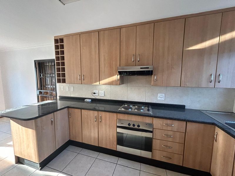 A functional kitchen featuring light wood-finish cabinetry, dark granite countertops, built-in oven, electric hob, and tiled flooring.