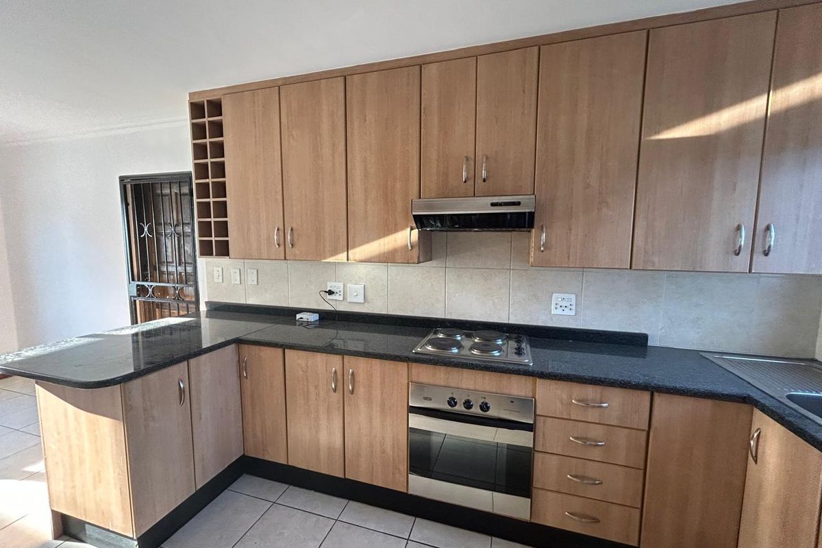 A functional kitchen featuring light wood-finish cabinetry, dark granite countertops, built-in oven, electric hob, and tiled flooring.