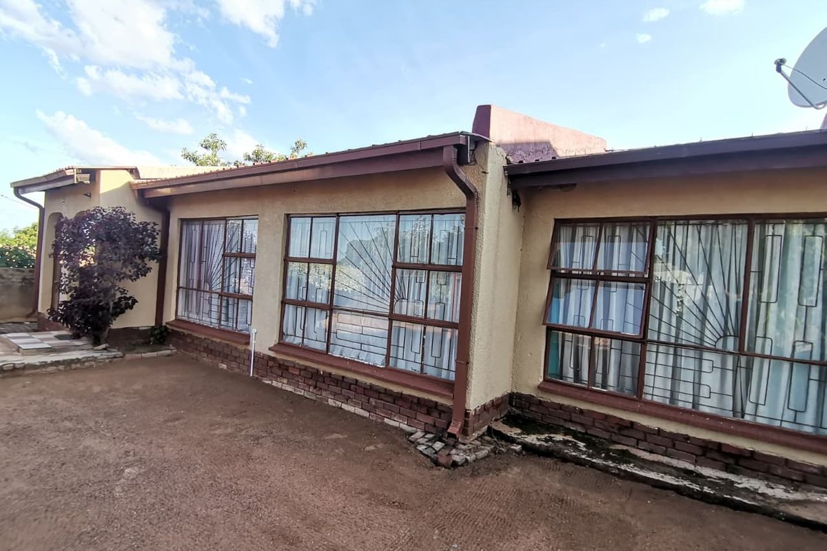 Rear exterior view of the house featuring large windows with security bars, brick base detailing, and guttering system.