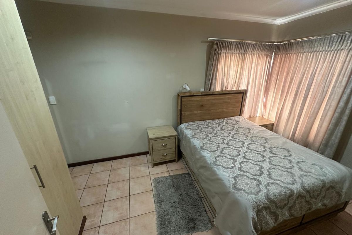 A functional bedroom featuring tiled flooring, built-in cupboard storage, and large windows with curtain rails, offering a neutral base for personalization.