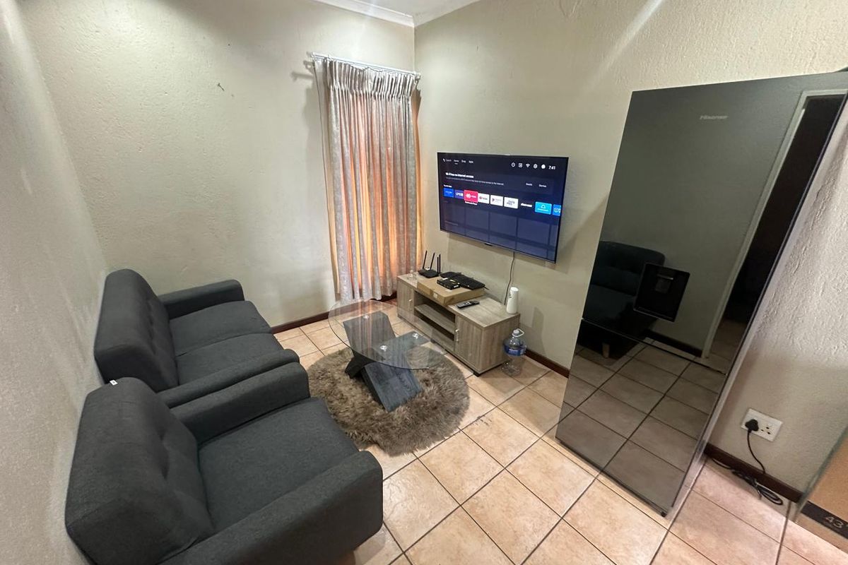 A compact living room featuring tiled flooring, coving, and wall-mounted television setup.