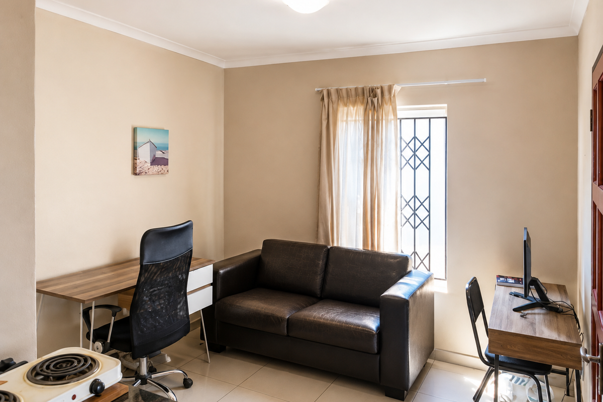 A functional living area featuring tiled flooring, neutral walls, and a window fitted with a security gate.