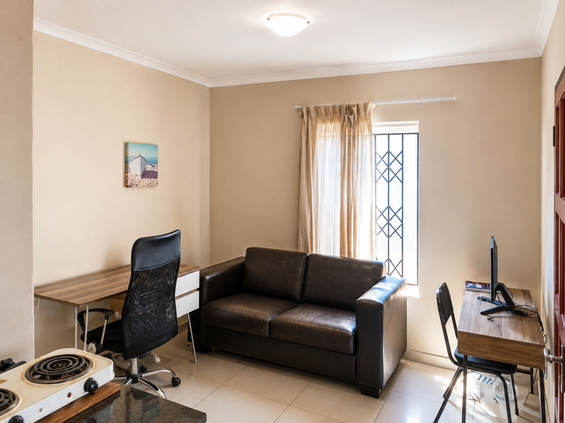 A functional living area featuring tiled flooring, neutral walls, and a window fitted with a security gate.
