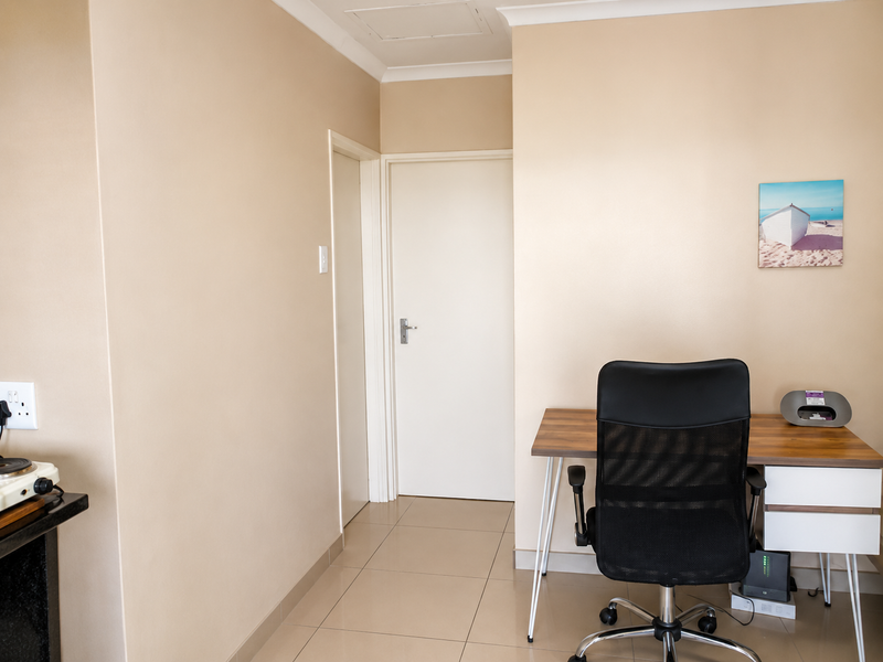 A functional office space featuring neutral wall tones, tiled flooring, and clean architectural lines, providing a versatile area for work or study.