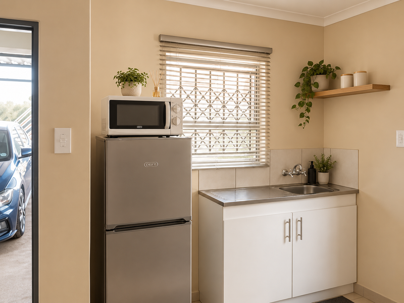 A compact scullery area featuring a stainless steel sink, built-in white cabinetry, and a window with venetian blinds, providing functional utility space.