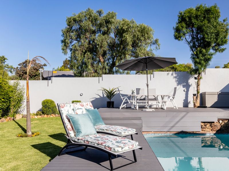 Outdoor pool area featuring a swimming pool, raised timber decking, and a secure perimeter wall with electric fencing.