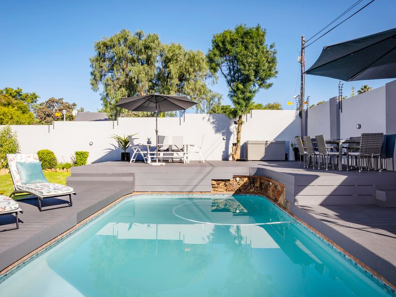 A well-maintained outdoor pool area featuring composite decking, a clear swimming pool, and a secure perimeter wall with electric fencing.