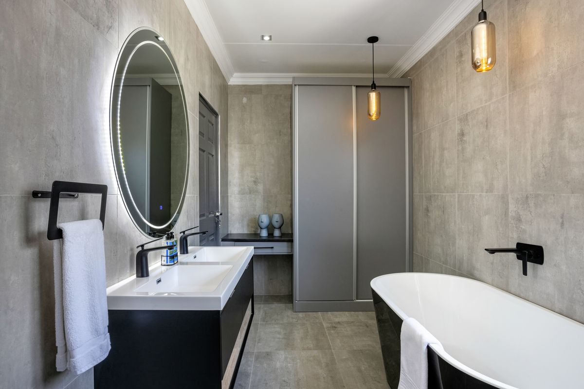 Modern bathroom featuring a double vanity, illuminated mirror, freestanding bathtub, and sleek grey tiled finishes with contemporary black fixtures.