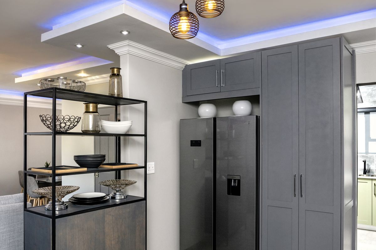 Modern kitchen area featuring sleek grey built-in cabinetry, contemporary pendant lighting, and ambient cove lighting, complemented by neutral tiled flooring.
