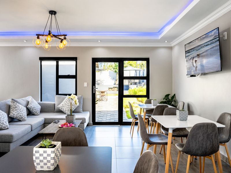 Modern open-plan living and dining area featuring tiled floors, recessed cove lighting, and direct access to the outdoor patio through glass doors.