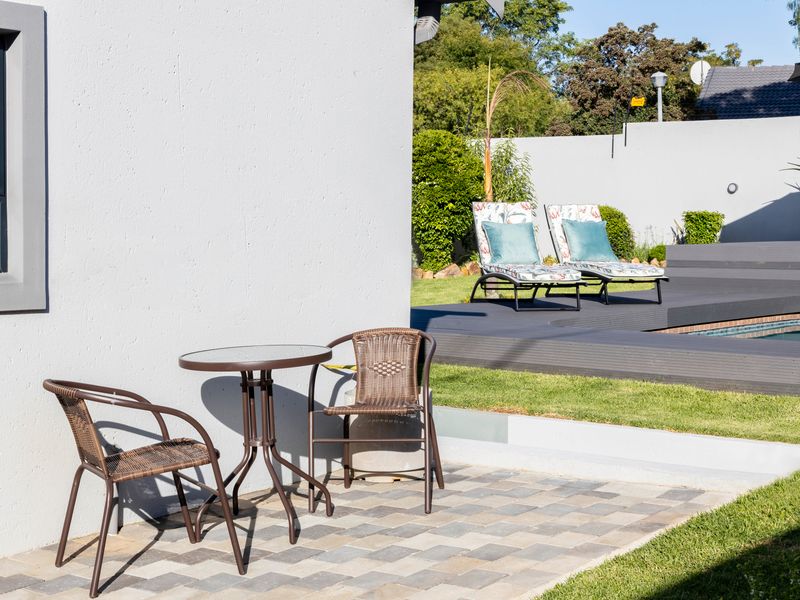 A well-maintained outdoor pool area featuring a paved patio, composite decking surrounding the pool, and a secure boundary wall.