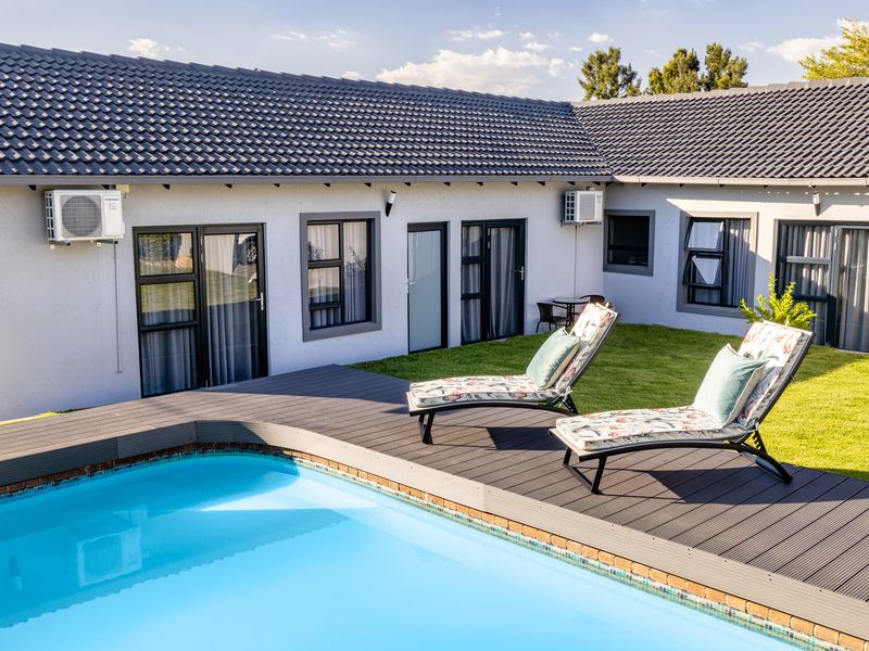 A well-maintained outdoor pool area featuring composite decking, a clear swimming pool, and modern aluminium-framed doors and windows leading into the home.