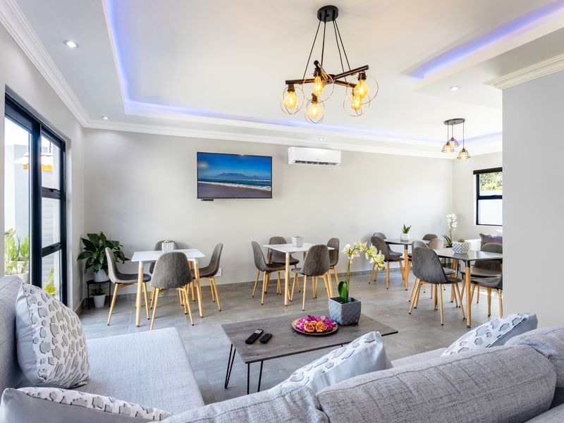 A modern, well-lit open-plan living and dining area featuring tiled floors, recessed ceiling lighting, and a wall-mounted air conditioning unit.