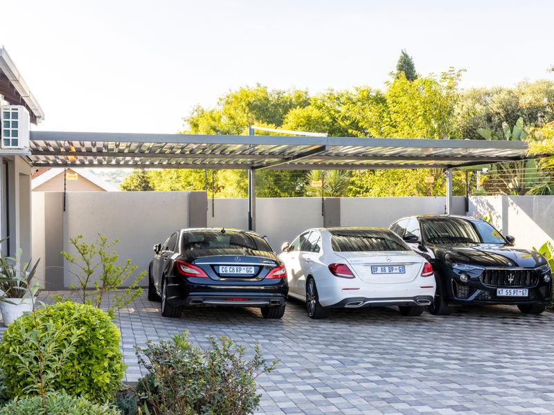 A modern, paved carport area featuring a sleek metal roof structure, perimeter walling with electric fencing, and an exterior air conditioning unit.