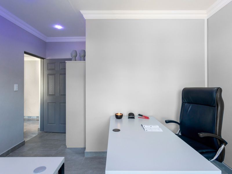 A modern, well-lit home office featuring neutral wall tones, crown molding, tiled flooring, and a clean, functional layout.