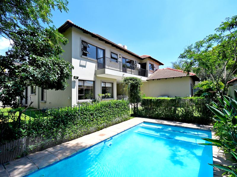 A well-maintained townhouse exterior featuring a private swimming pool, landscaped garden, and an upper-level balcony with sliding door access.