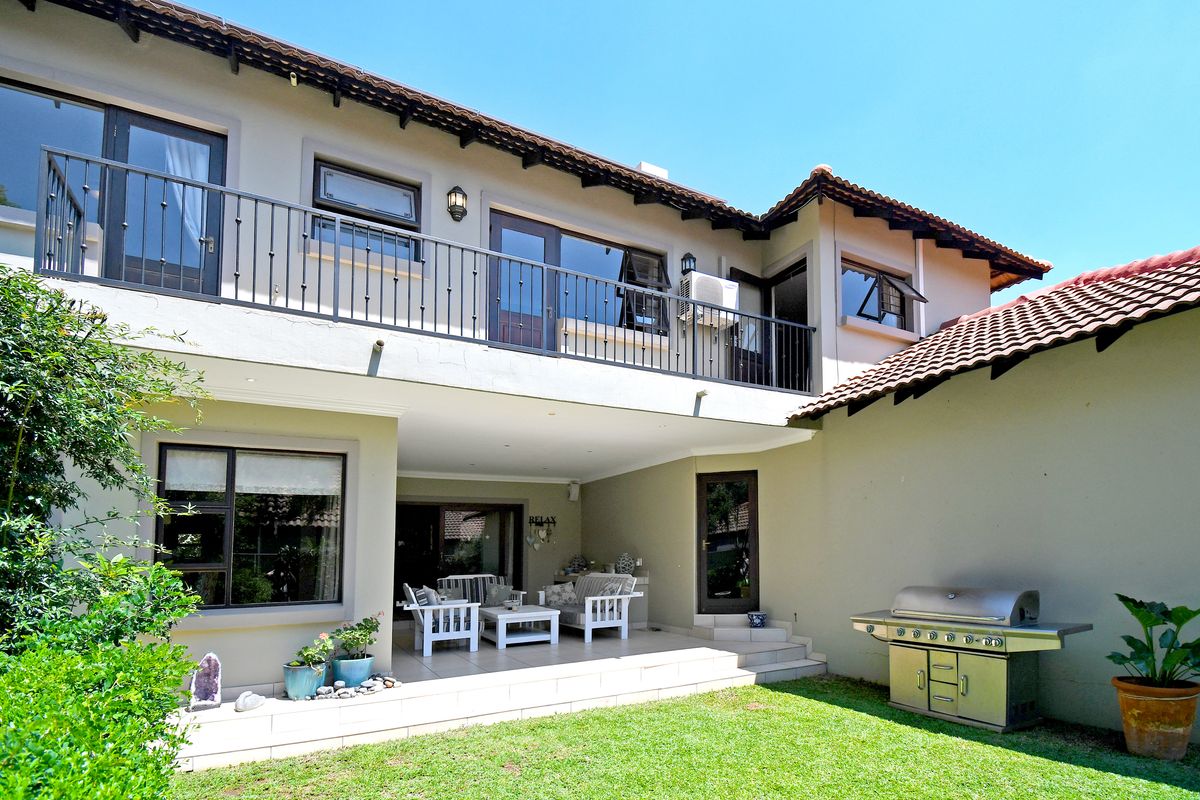 Rear view of the townhouse featuring a covered tiled patio, upper-level balcony with iron railings, and a built-in outdoor braai area.