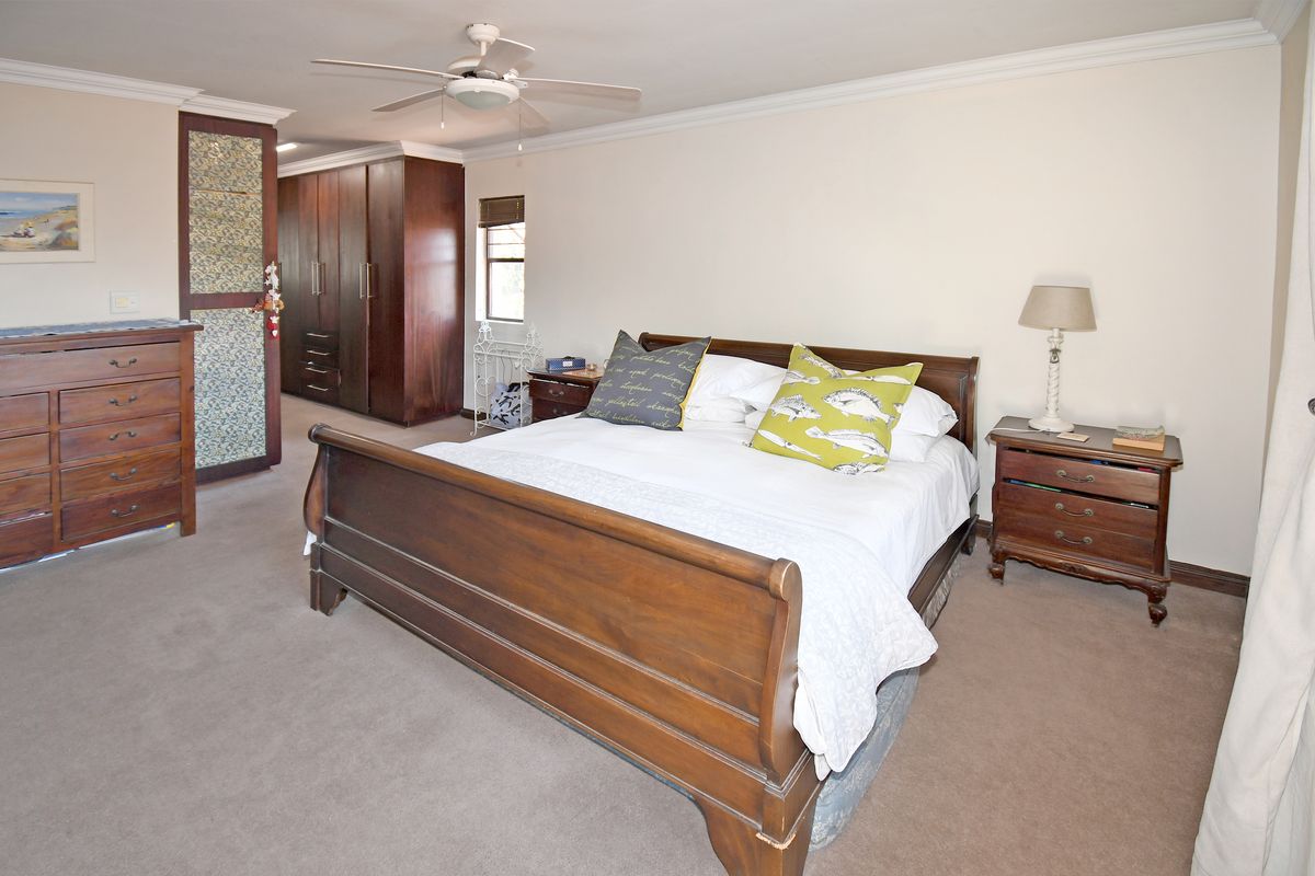 Spacious bedroom featuring built-in wooden cupboards, neutral carpeting, and a ceiling fan, offering a comfortable and functional living space.