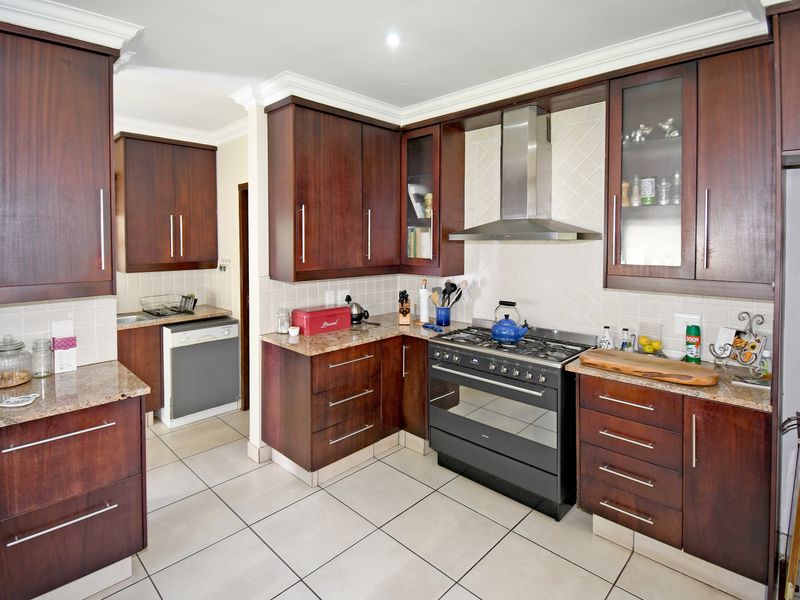 A well-maintained kitchen featuring dark wood cabinetry, granite countertops, a gas stove with extractor fan, and neutral tiled flooring.