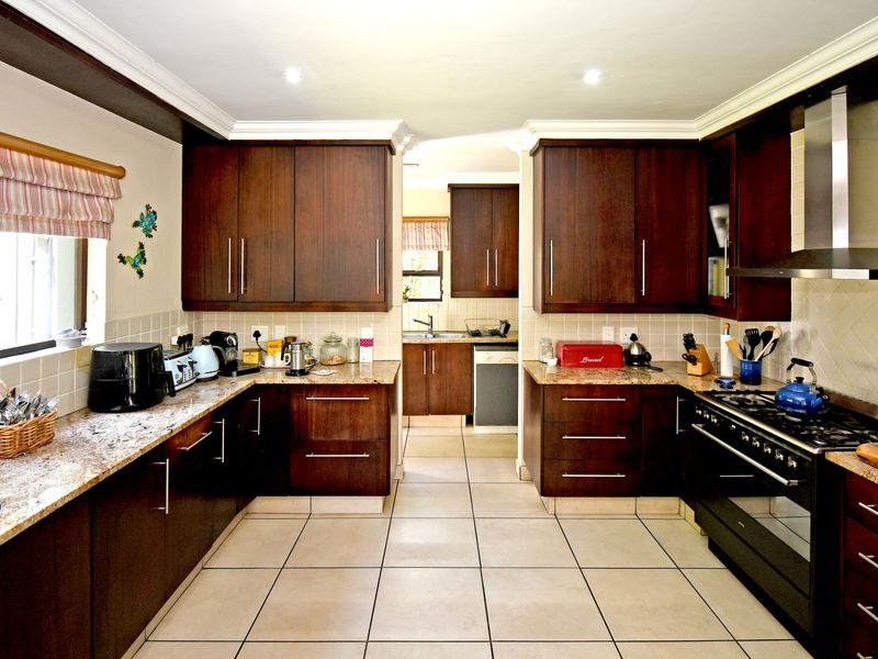 A well-maintained kitchen featuring dark wood cabinetry, granite countertops, a gas hob with extractor fan, and tiled flooring with a functional scullery area.