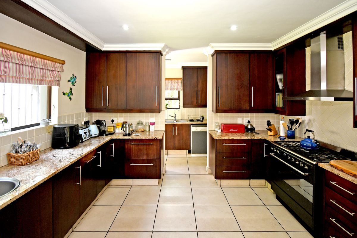 A well-maintained kitchen featuring dark wood cabinetry, granite countertops, a gas hob with extractor fan, and tiled flooring with a functional scullery area.