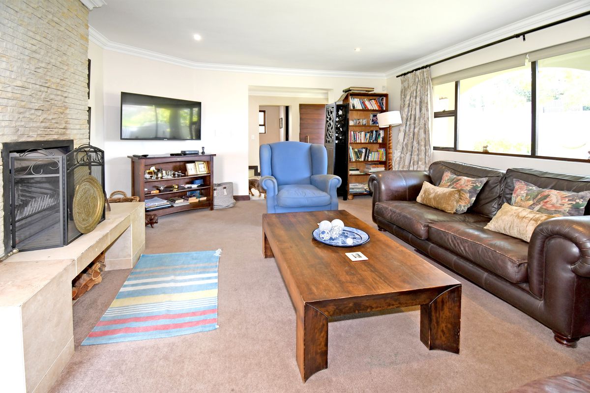 Spacious living room featuring a prominent stone fireplace, neutral carpeting, crown molding, and large windows providing ample natural light.
