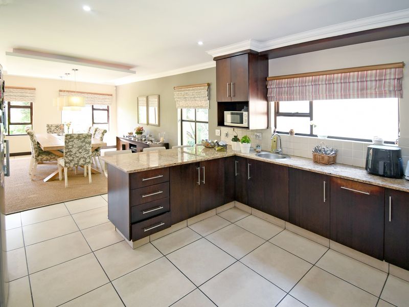 Open-plan kitchen and dining area featuring dark wood cabinetry, granite countertops, tiled flooring, and ample natural light.