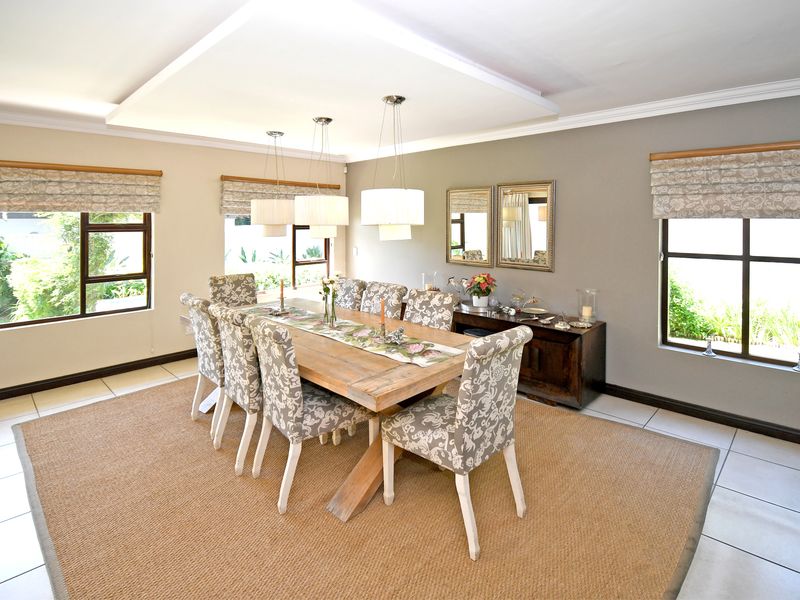 A bright and spacious dining room featuring tiled flooring, recessed ceiling lighting, and large windows with fitted roman blinds.