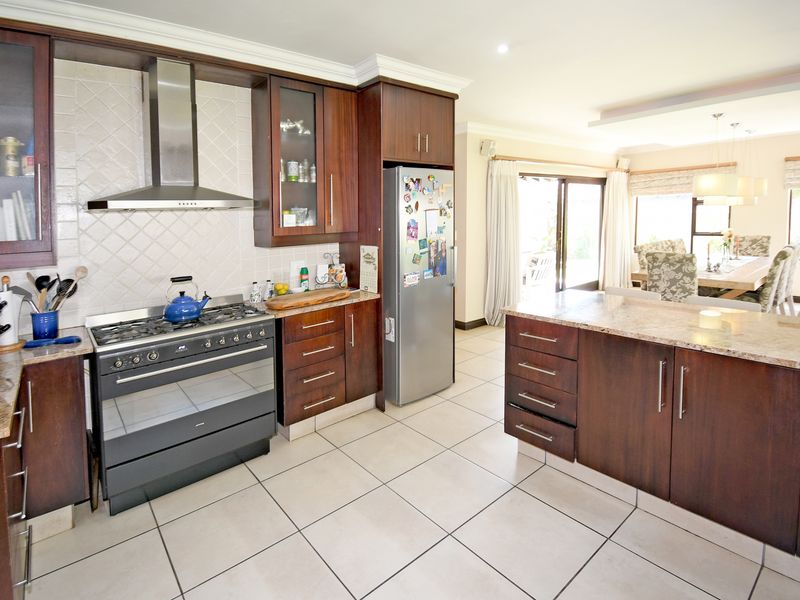 Open-plan kitchen featuring dark wood cabinetry, granite countertops, a gas stove with extractor fan, and a central island, flowing into the dining area.
