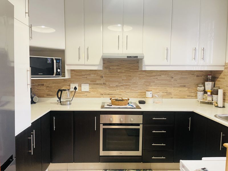 Modern kitchen featuring high-gloss white upper cabinets, dark lower cabinetry, stone countertops, and integrated stainless steel appliances including an oven and extractor fan.