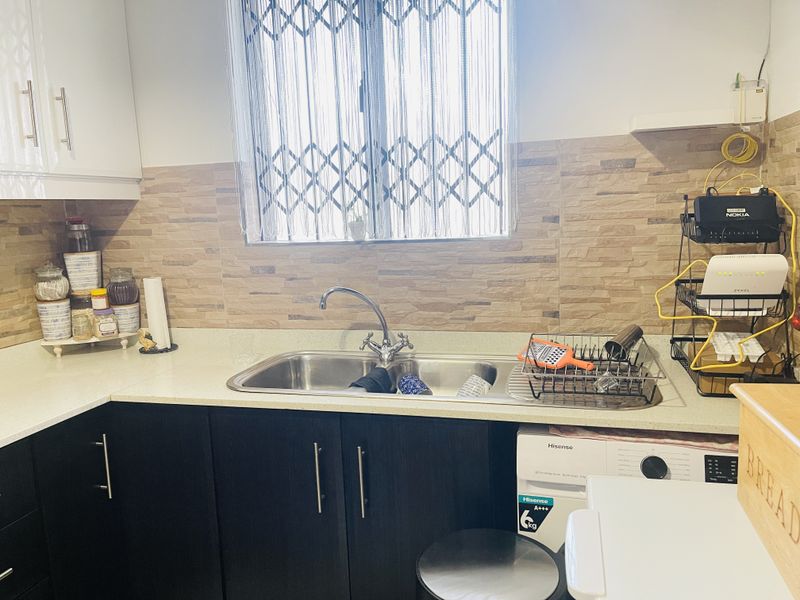 A functional kitchen area featuring dark cabinetry, stone countertops, a stainless steel double sink, and a decorative tiled backsplash.