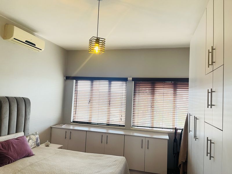 A well-maintained bedroom featuring built-in cupboards, additional under-window cabinetry, venetian blinds, and a wall-mounted air conditioning unit.