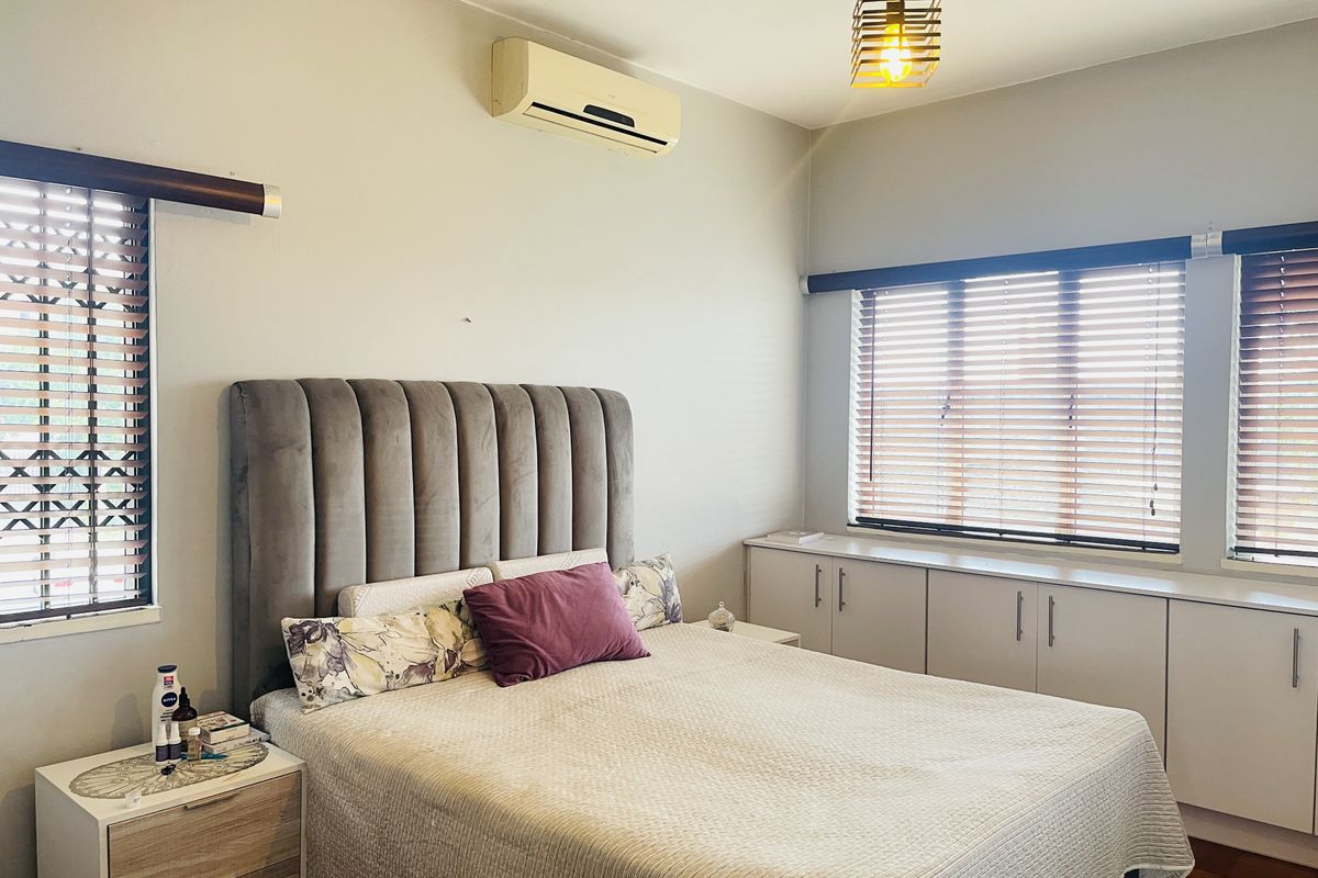 A well-lit bedroom featuring built-in storage cabinetry, venetian blinds, and a wall-mounted air conditioning unit.