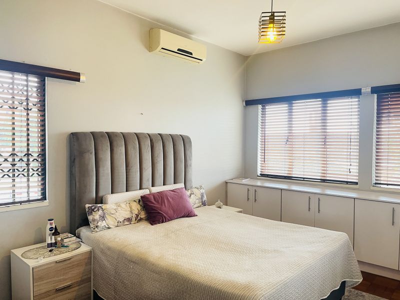 A well-lit bedroom featuring built-in storage cabinetry, venetian blinds, and a wall-mounted air conditioning unit.