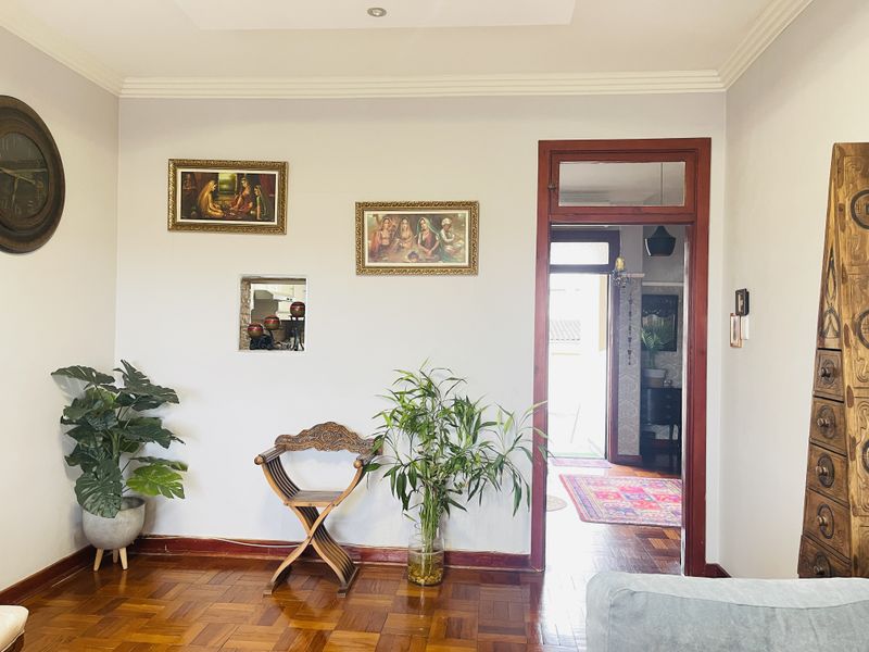 A well-maintained living room featuring classic parquet flooring, decorative cove ceiling molding, and a unique recessed wall niche, leading into an adjacent hallway.