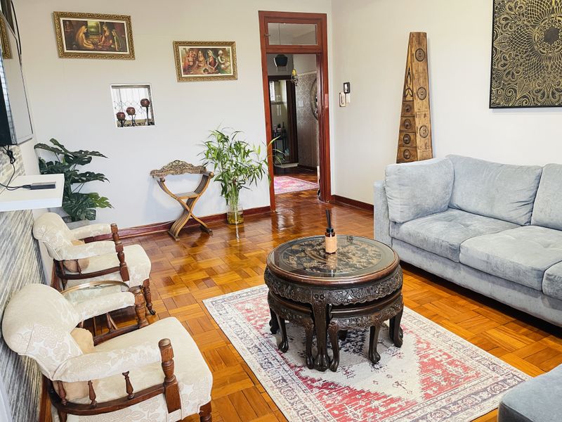 A well-maintained living room featuring classic parquet flooring and a distinct wooden door frame leading to an adjacent hallway.