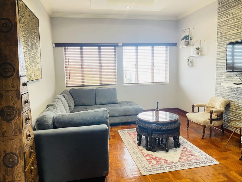 A well-maintained living room featuring warm parquet flooring, a textured stone feature wall, and recessed ceiling lighting with natural light from venetian blinds.