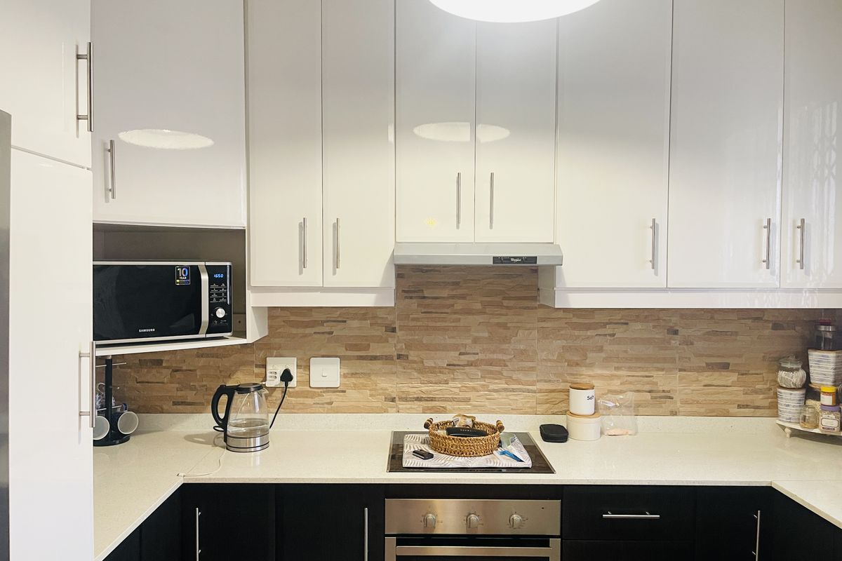Modern kitchen featuring high-gloss white upper cabinets, dark lower cabinetry, stone countertops, and a textured stone tile backsplash with integrated appliances.