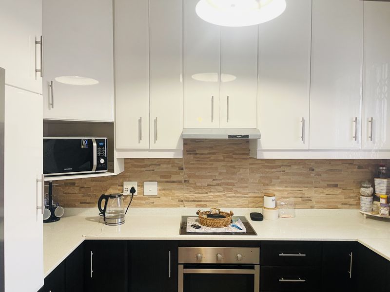 Modern kitchen featuring high-gloss white upper cabinets, dark lower cabinetry, stone countertops, and a textured stone tile backsplash with integrated appliances.