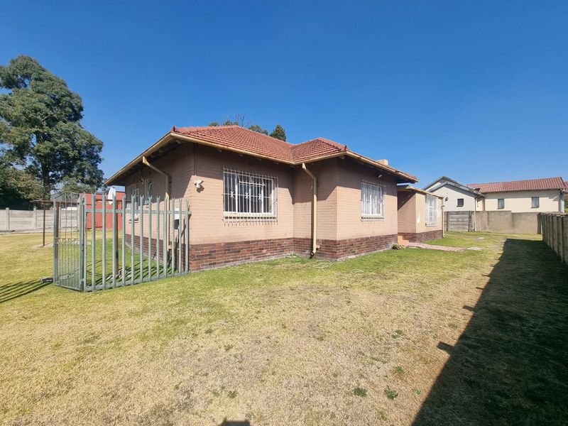 Rear view of a single-story brick house featuring a tiled roof, security bars on windows, and a fenced garden area.