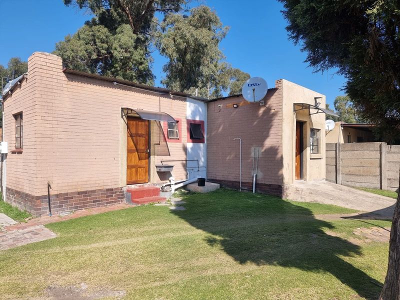 Rear view of a brick house featuring a small lawn, satellite dishes, and external access doors with protective awnings.