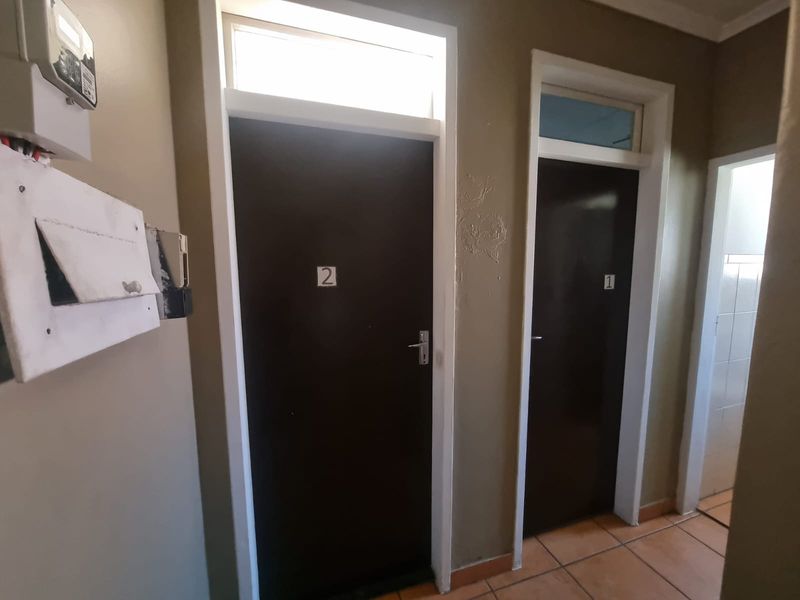 A functional hallway featuring tiled flooring, two numbered doors with transom windows, and a wall-mounted electrical distribution board.