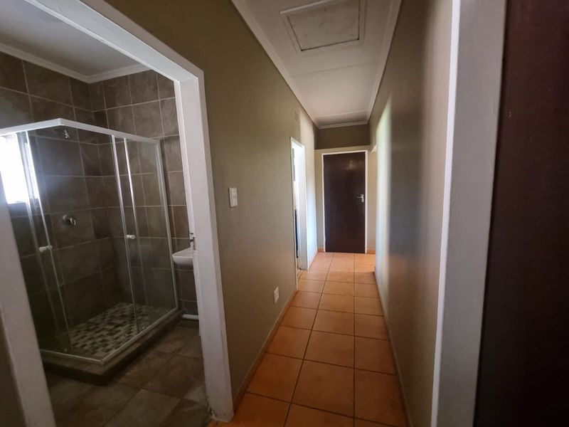 A functional hallway featuring tiled flooring and direct access to an adjacent bathroom equipped with a shower enclosure and wall-mounted basin.