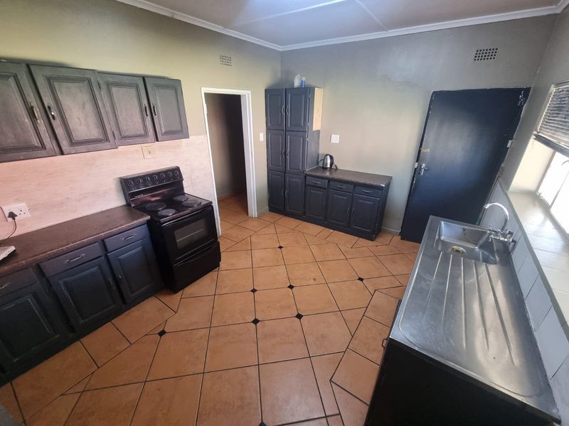 A functional kitchen featuring dark cabinetry, an electric stove, stainless steel sink, and tiled flooring, offering potential for a modern cosmetic update.