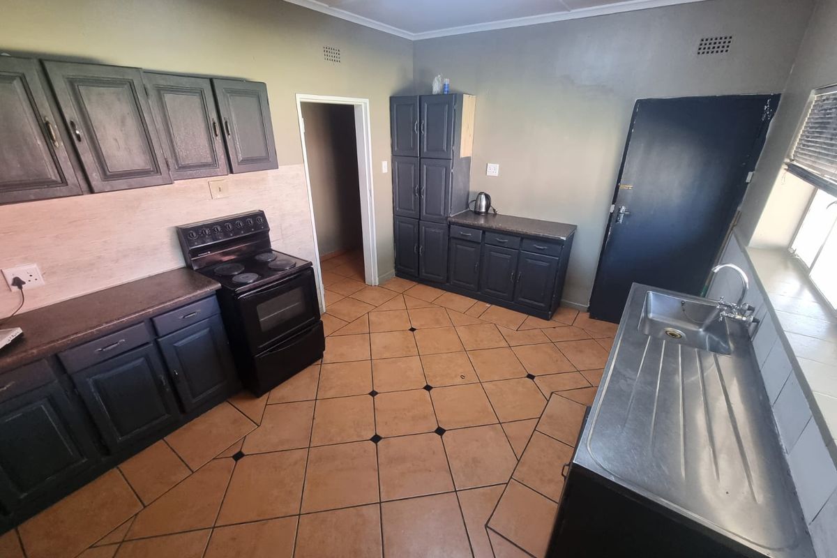 A functional kitchen featuring dark cabinetry, an electric stove, stainless steel sink, and tiled flooring, offering potential for a modern cosmetic update.