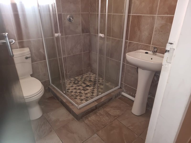 A functional bathroom featuring a shower enclosure, pedestal basin, and toilet with tiled finishes throughout.