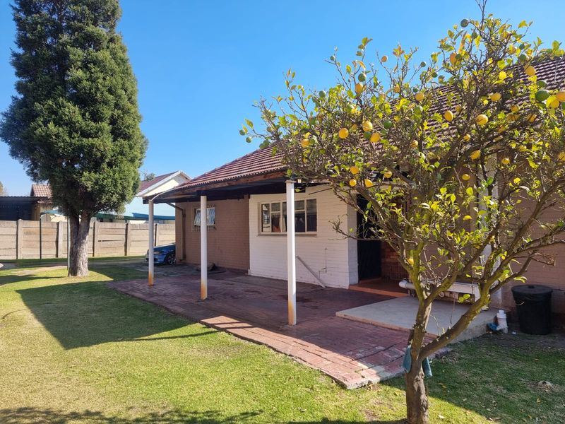 Rear view of the property featuring a brick patio, covered veranda with metal support columns, and a well-maintained garden area.