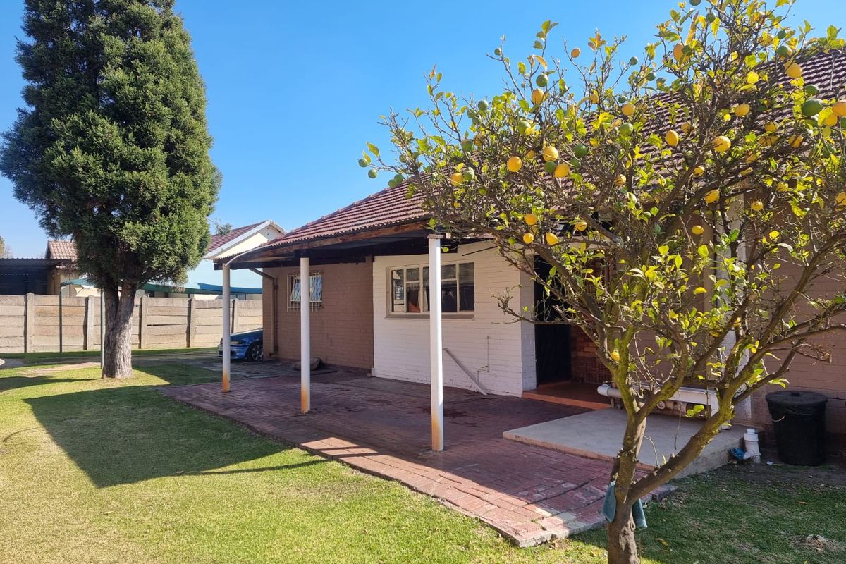 Rear view of the property featuring a brick patio, covered veranda with metal support columns, and a well-maintained garden area.