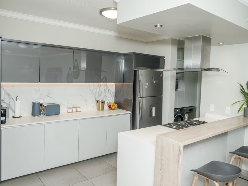 Modern kitchen featuring high-gloss grey cabinetry, marble-look splashback, stone countertops, and a breakfast bar with an integrated gas hob and extractor fan.