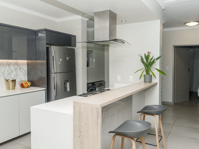 Modern kitchen featuring sleek grey and white cabinetry, stone countertops, a breakfast bar, and integrated stainless steel appliances.